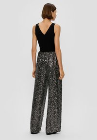Schwarzer ärmelloser Body mit V-Ausschnitt, kombiniert mit weit geschnittenen Pailletten-Hosen in Schwarz und Silber, die Textur und Glanz hinzufügen.