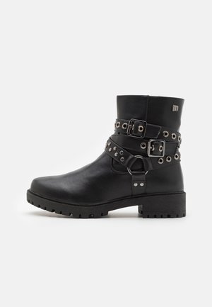 Bottine noire à cheville avec petit talon, semelle robuste, double boucle décorative et brides cloutées autour de la tige sur fond uni.