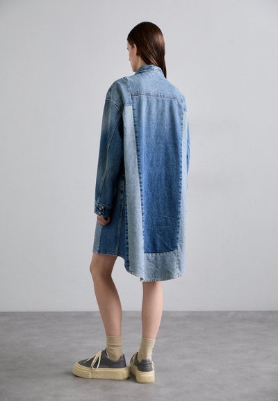 Denima jaka kleita dažādos zila toņos, ar garām piedurknēm, sānu kabatām un garāku aizmugurējo paneli. Kombinēta ar sportiskām platformas kurpēm.