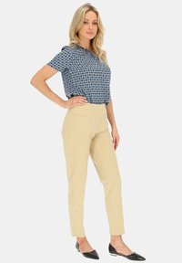 Niebieska bluzka z krótkim rękawem w wzory, z wysokim kołnierzem, zestawiona z jasnobeżowymi spodniami o kroju dopasowanym i czarnymi czółenkami z owalnym noskiem.