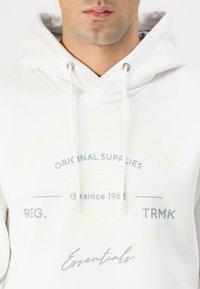 Weißer Hoodie mit Kordelzug, präsentiert hellgrüne und graue grafische Schriftzüge auf der Vorderseite. Weicher Stoff, lässiges Design, normale Passform.