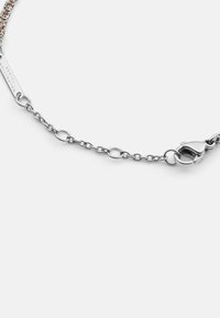 Bracciale in argento con lunghezza regolabile. Design a maglie con chiusura a moschettone e targhetta incisa. Accentuato da piccole cristalli trasparenti.