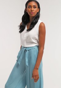 White sleeveless top with a textured finish, paired with light blue wide-leg pants featuring a tied waistband. Simple and relaxed fit.