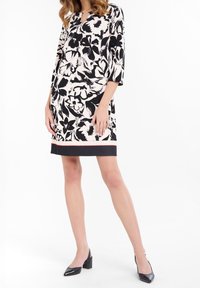 Robe fleurie en noir et blanc, avec un col rond, des manches trois-quarts et un ourlet noir contrastant avec une bande rouge.