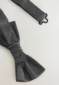 Black fabric bow tie featuring white dotted pattern, adjustable strap, and a black plastic fastening clip. Smooth texture and symmetrical shape.