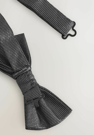 Sort stof butterfly med hvidt prikmønster, justerbar rem og spænde i sort plast. Glat tekstur og symmetrisk form.