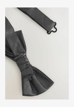 Sort stof butterfly med hvidt prikmønster, justerbar rem og spænde i sort plast. Glat tekstur og symmetrisk form.