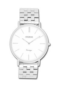 Montre en acier inoxydable argenté avec un cadran rond blanc. Présente des index horaires fins, un logo minimaliste et un bracelet en maillons métalliques.