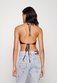 Černý halter bikiny top s růžovým a fialovým květinovým vzorem; spárovaný s vysokým pasem světle modrými denimovými džíny s vyšitými logy.