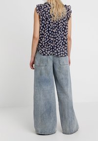 Blusa floreale navy con maniche arricciate abbinata a jeans svasati azzurri chiari con due tasche posteriori e una finitura morbida e testurizzata.