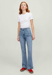 Jeans de denim azul claro, de boca larga, com cintura alta, lavagem desbotada e silhueta reta, combinados com uma t-shirt branca justa e sapatos vermelhos.