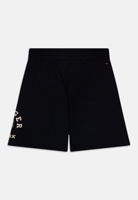 Zwarte katoenen shorts met een elastische tailleband hebben een crèmekleurige logo-opdruk op het linkerbeen. Het ontwerp is klassiek en eenvoudig, met een gladde textuur.