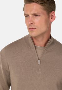 Beiger Halb-Reißverschluss-Pullover aus strukturiertem Stoff. Mit Stehkragen und subtilen Nahtdetails, die ein lässiges, aber ordentliches Design unterstreichen.