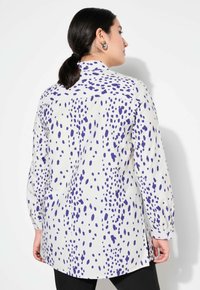Camicia bianca a maniche lunghe con un motivo a pois viola, dal taglio rilassato, con spacco laterale e colletto a punta.