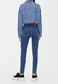 Chaqueta de mezclilla con diseño recortado, color azul claro, dobladillo deshilachado, combinada con jeans ajustados azules, vista posterior, zapatillas de plataforma negras.
