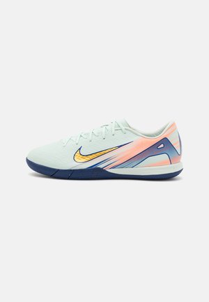 Chaussure de sport vert clair avec une tige texturée, semelle marine et accents en dégradé de corail et de bleu. Présente un grand logo swoosh doré.
