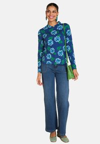 Long-sleeve blue top with floral pattern, paired with wide-leg blue jeans and green handbag. Green and white striped flats complete the look.