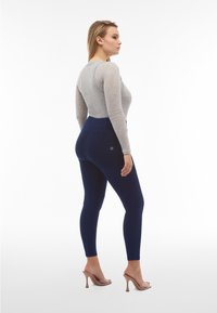 Leggings a vita alta in denim elasticizzato blu navy, con cuciture in tono e una tasca posteriore, abbinati a un top a maniche lunghe grigio chiaro.