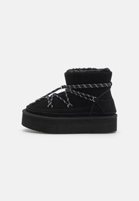Botas de tobillo de ante negro con suela gruesa de plataforma negra, con forro de felpa, cordones entrelazados y detalles de hardware en plata.