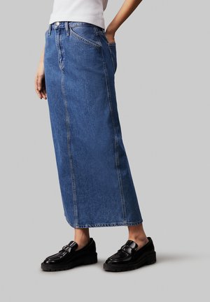 Denim maxi rok in medium blauw met een rechte vorm, voorzakken en een rauwe zoom. Gepaard met zwarte zware loafers.
