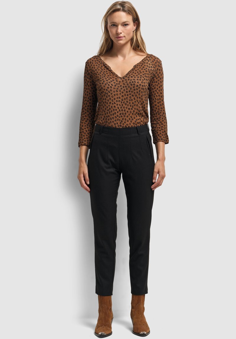 Haut à imprimé léopard marron avec un décolleté en V et des manches trois quarts, associé à un pantalon noir plissé et des bottines à talons en daim marron.