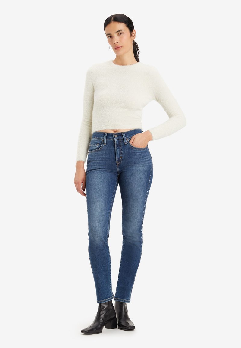 Pullover bianco corto con una finitura testurizzata abbinato a jeans blu scuro a vestibilità slim. Il modello indossa stivali neri fino alla caviglia. Design e vestibilità semplici.