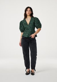 Groene blouse met een patroon, puffmouwen, diepe v-hals en een cinched taille. Gecombineerd met donkere broeken en zwarte puntige schoenen. Fijne stof textuur.