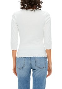 Witte, ribbelige top met driekwart mouwen en een gegolfde onderrand en halslijn, gecombineerd met lichtblauwe, high-waisted jeans met achterzakken.