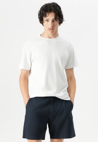 Tricou alb din bumbac, cu guler rotund și mâneci scurte, asortat cu pantaloni șort bleumarin, cu buzunare laterale și o croială lejeră.
