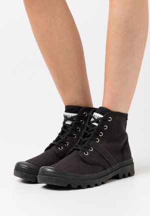 Bottines noires en toile avec une semelle en caoutchouc texturée, des œillets en métal et des lacets noirs contrastants. Elles sont dotées d'un col rembourré et d'un accent de logo.
