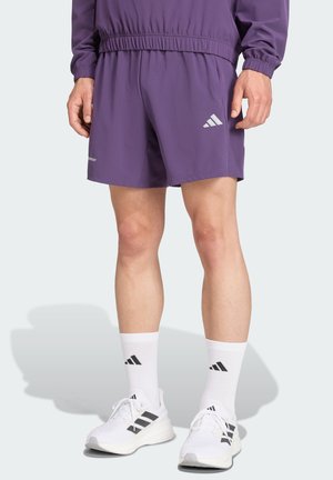 Lilla træningsshorts med elastisk talje, prydet med reflekterende detaljer og et logo. Sæt sammen med hvide sokker og sko med sorte striber.