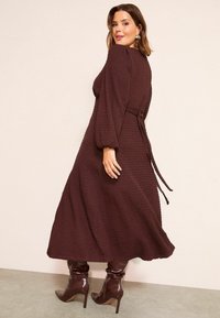 Rochie lungă maro, cu textură, mâneci bufante și talie cu cordon. Asortată cu cizme maro cu toc înalt, lucioase, cu finisaj neted.