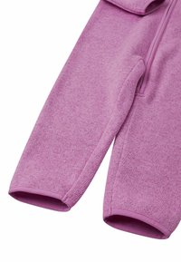 Spodnie z polaru w miękkim jasnoróżowym kolorze, z gładką teksturą i dopasowanymi mankietami. Widoczne przeszycia wzdłuż boków.