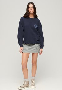 Felpa in cotone blu navy con scollo rotondo e grafica frontale, abbinata a una gonna cargo grigia lunga fino al ginocchio con tasche.
