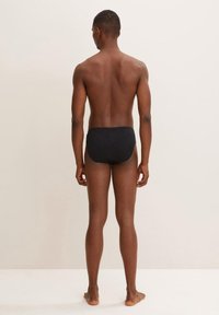 Slip da bagno neri realizzati in un materiale elastico, con un design senza cuciture e un taglio moderato, visti dal retro senza accenti visibili.
