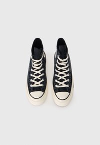 Sneakers negre cu guler înalt, realizate din material texturat, cu șireturi albe și o talpă din cauciuc de culoare crem, având un vârf în contrast.
