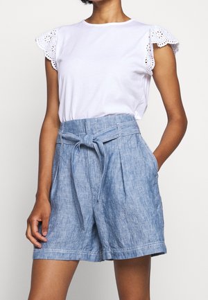 T-shirt bianco a maniche corte con spalle in pizzo, abbinato a pantaloni corti in misto lino blu chiaro con cintura a fiocco e fronte plissettata.