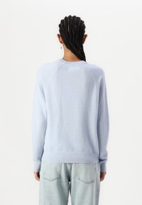 Suéter de punto suave en azul claro con mangas raglán y puños acanalados. Textura lisa, con un diseño minimalista y un escote redondeado.