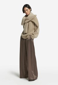 Beżowy sweter dzianinowy z szerokim kołnierzem, zestawiony z brązowymi satynowymi spodniami typu wide-leg. Sweter ma ściągacze na rękawach i luźny krój.