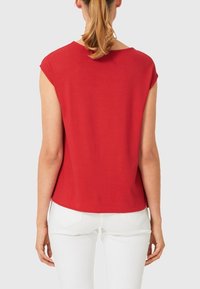 Rød kortærmet top med rund halsudskæring. Blødt, glat stof med en afslappet pasform. Bagkanten er let længere end fortil.