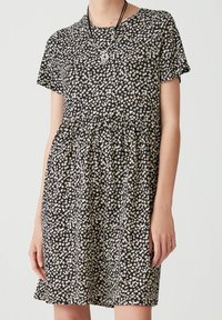 Schwarzes kurzärmeliges Kleid mit einem floralem Muster in Weiß und Gelb. Ausgestellter Rock mit gerafftem Bund, aus leichtem Stoff gefertigt.