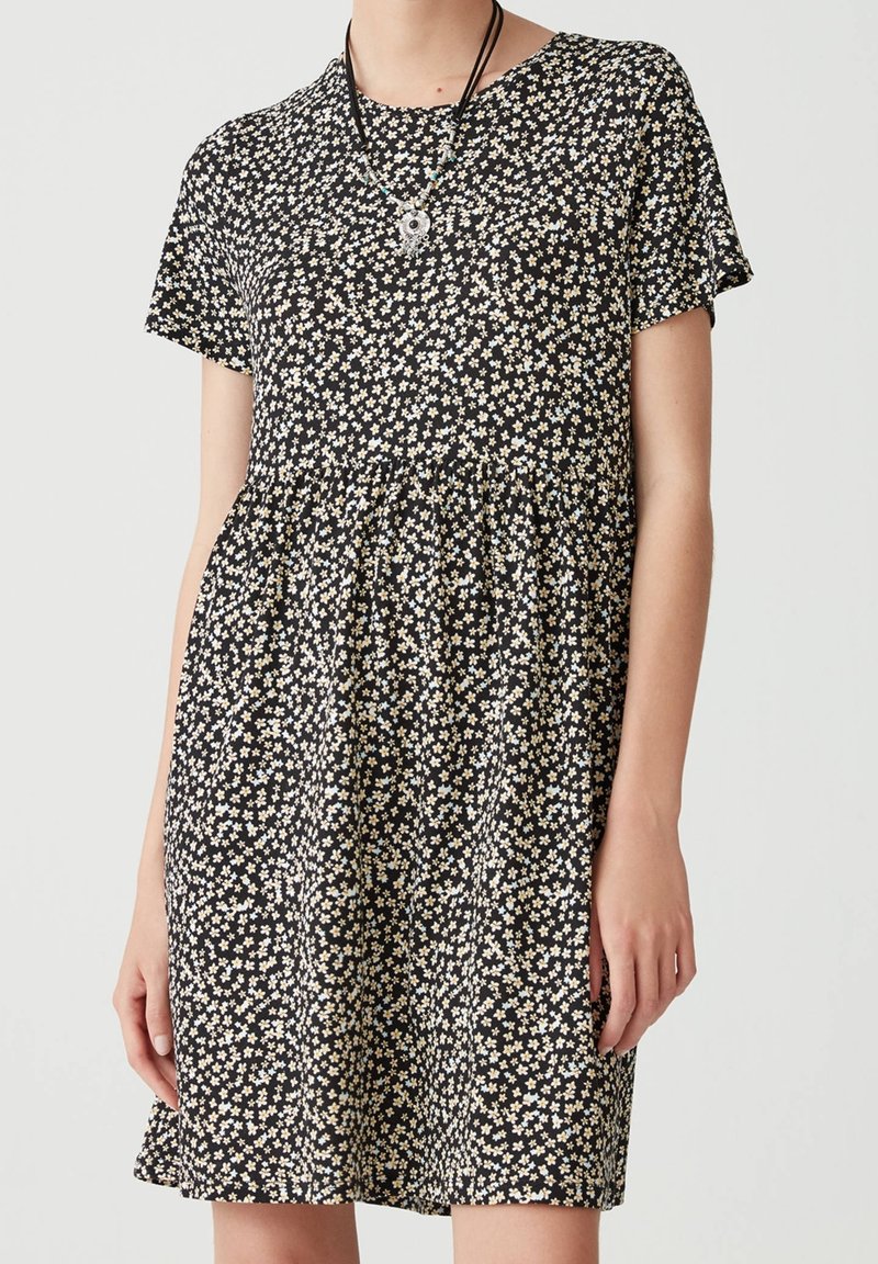 Schwarzes kurzärmeliges Kleid mit einem floralem Muster in Weiß und Gelb. Ausgestellter Rock mit gerafftem Bund, aus leichtem Stoff gefertigt.