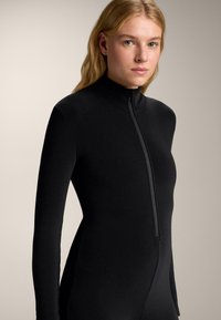 Čierne priliehavé body s vysokým golierom a dlhými rukávmi, s predným zipsom. Jemná textúra látky, minimalistický dizajn.