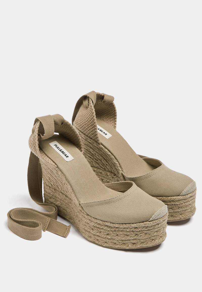 Beige Leinenschuhe mit Keilabsätzen, einer strukturierten Espadrille-Sohle, runder Zehenpartie und schmalen Riemen um den Knöchel. Mit einer Schleifendetails auf der Rückseite.