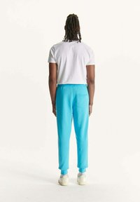 Turquoise joggingbroek in een relaxte pasvorm, met geribbelde boorden en een achterzak. Gecombineerd met een eenvoudig wit t-shirt.