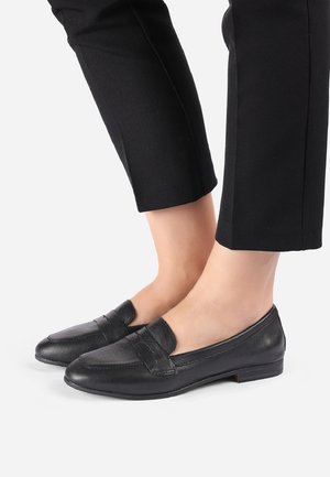 Sorte læder loafers med rund tå, med en stropdetalje henover toppen, lav hæl og glat tekstur. Bæres med sorte cropped bukser.