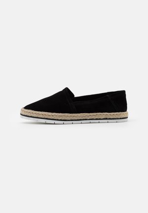 Chaussure slip-on en daim noir avec un contour en jute tressé et une semelle en caoutchouc blanc, dotée d'un design à bout pointu et de détails de coutures minimalistes.