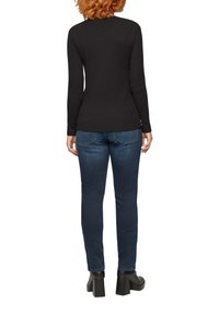 Schwarzes Langarmtop aus weichem Stoff, kombiniert mit eng anliegenden dunkelblauen Jeans und schwarzen Stiefeln mit dicken Absätzen. Schlichtes, figurbetontes Design.