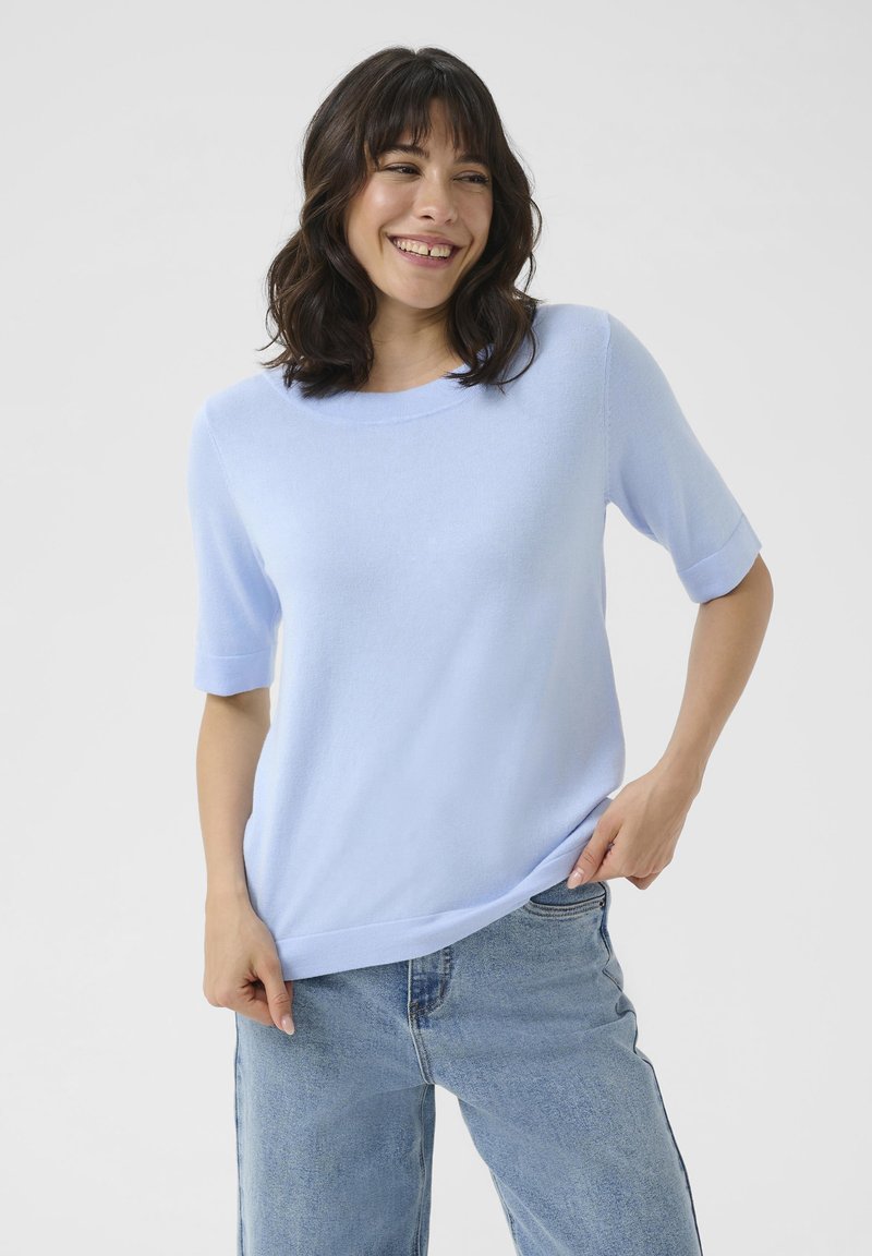 Pull bleu clair à manches courtes en tissu doux, avec un col rond et une coupe décontractée. Associé à un jean bleu clair.