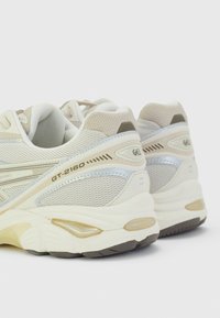 Béžové běžecké boty s texturovaným síťovaným svrškem a gumovou podrážkou. Mají stříbrné detaily a nápis "GT-2160" na boku.